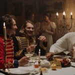 men in british military costumes sitting by the table having a feast