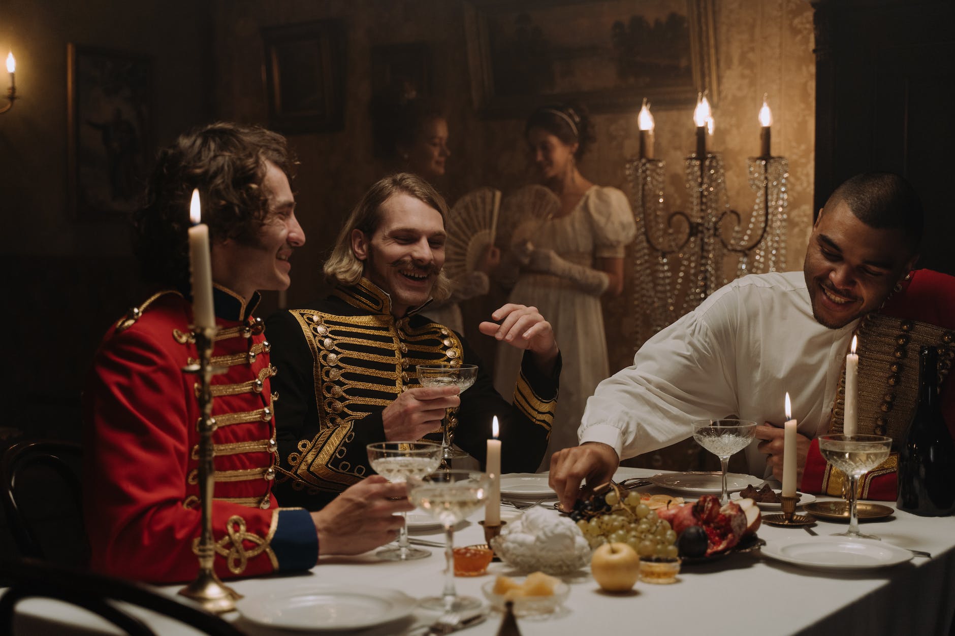 men in british military costumes sitting by the table having a feast